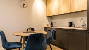 A modern kitchen with a round table, two blue chairs, wooden cabinets, and a clock on the wall.