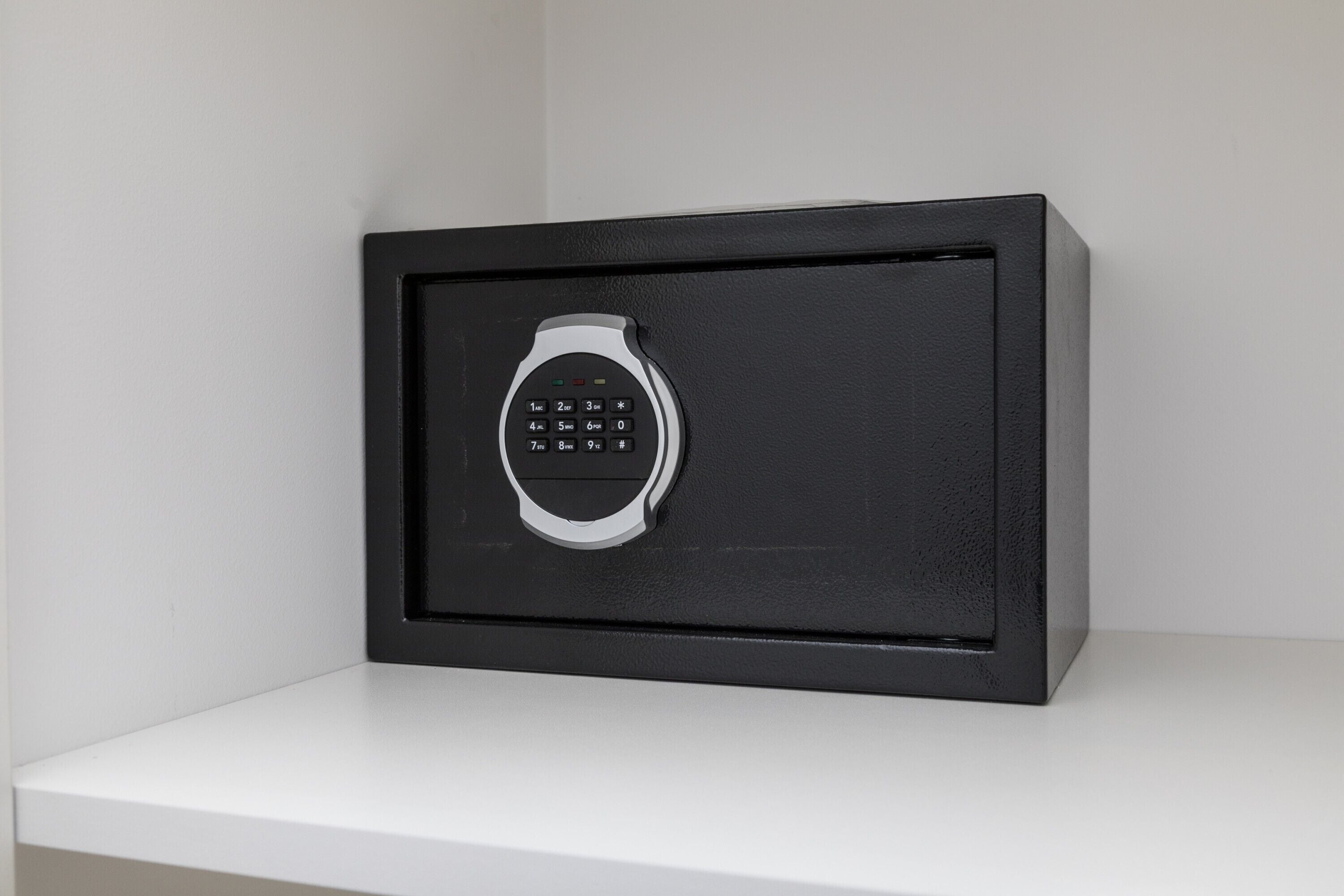 A black safe with a keypad on a white shelf.