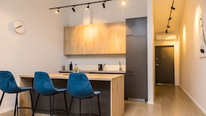 Une cuisine moderne avec des meubles en bois, un réfrigérateur noir et un coin bar avec des chaises bleues.