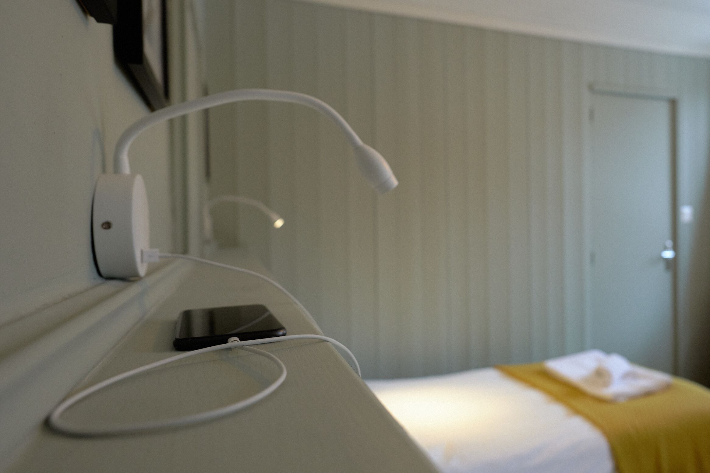 Une chambre d’hôtel avec un lit, une table de chevet avec une lampe et une prise de courant fixée au mur.