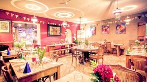Un restaurante con mesas y sillas de madera, paredes rojas e iluminación decorativa.