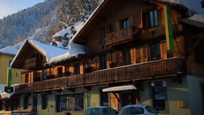 Una cabaña de madera con balcones, rodeada de árboles cubiertos de nieve y montañas.