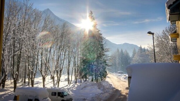 Un paisaje montañoso nevado con cielo despejado y un sol brillante.