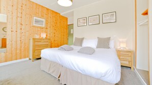 Un dormitorio con pared de madera, una cama con ropa de cama blanca, una mesita de noche con lámpara y un espejo.