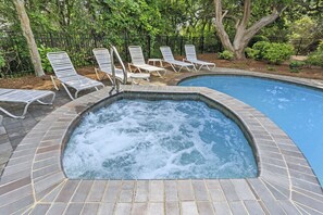 Un bain à remous entouré de chaises longues et d’une piscine, le tout aménagé dans un jardin paysager agrémenté d’arbres et d’une clôture.
