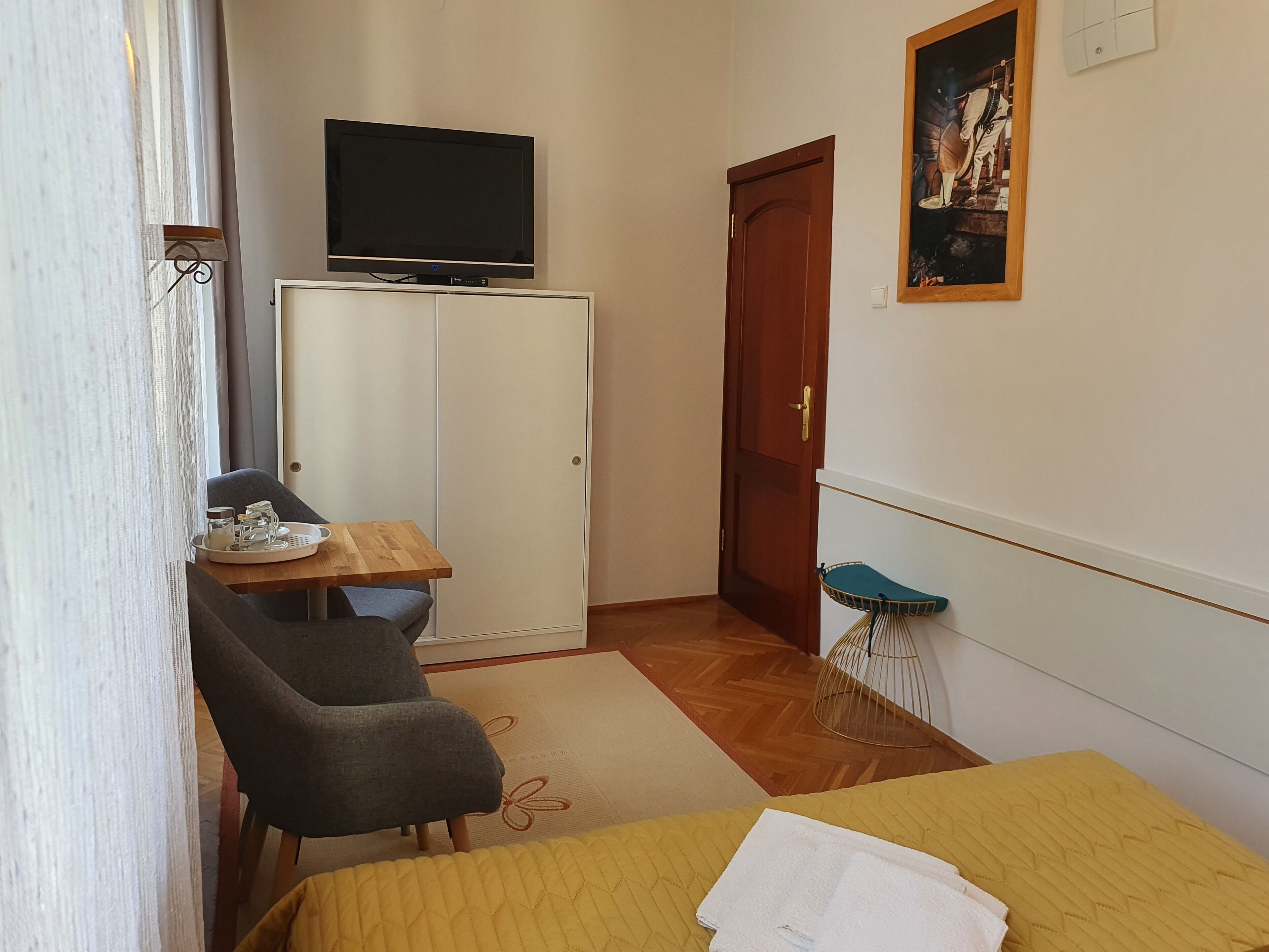 Una habitación pequeña con cama, escritorio, silla, televisor y puerta.