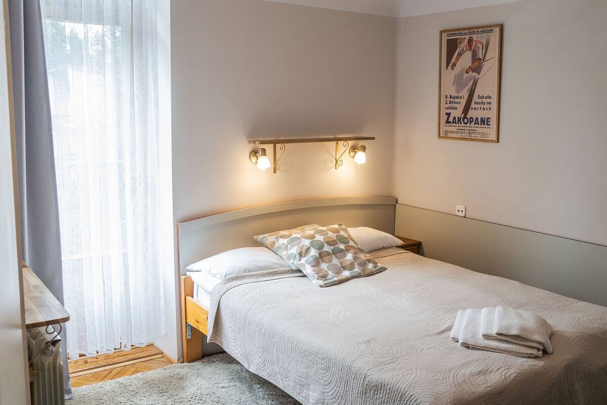 A neatly made bed with a patterned pillow, a bedside lamp, and a poster on the wall.