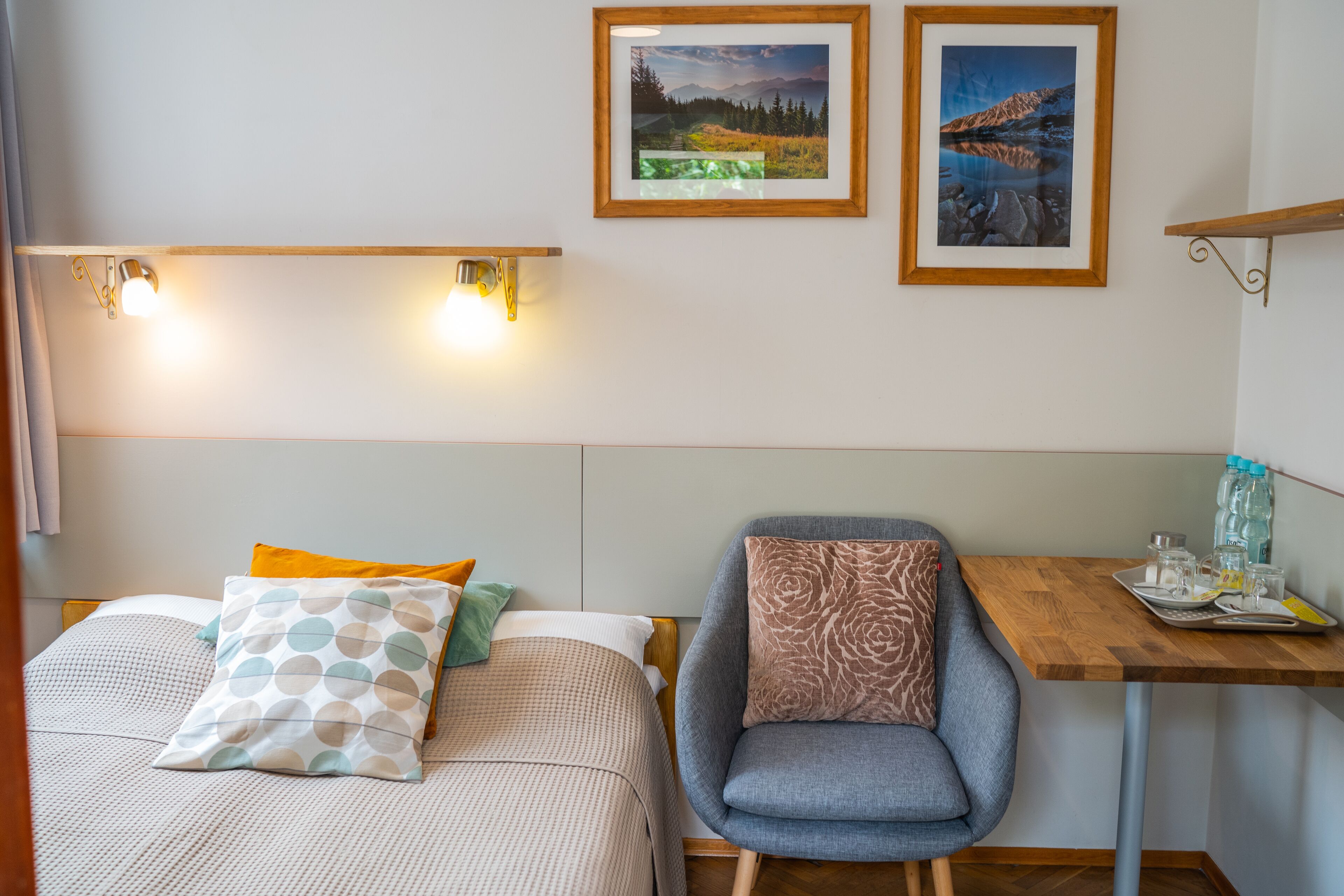 A hotel room with two beds, a chair, a small table with a tray, and two framed pictures on the wall.