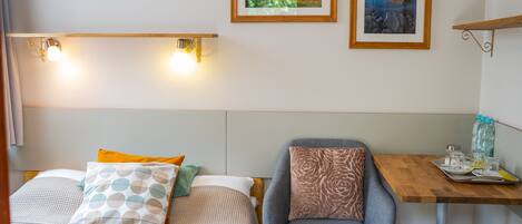 Habitación de hotel con dos camas, una silla, una mesita con bandeja y dos cuadros en la pared.