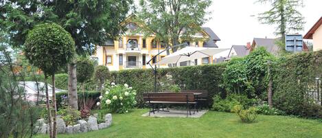 A well-maintained garden with a bench, a hedge, and a yellow building in the background.