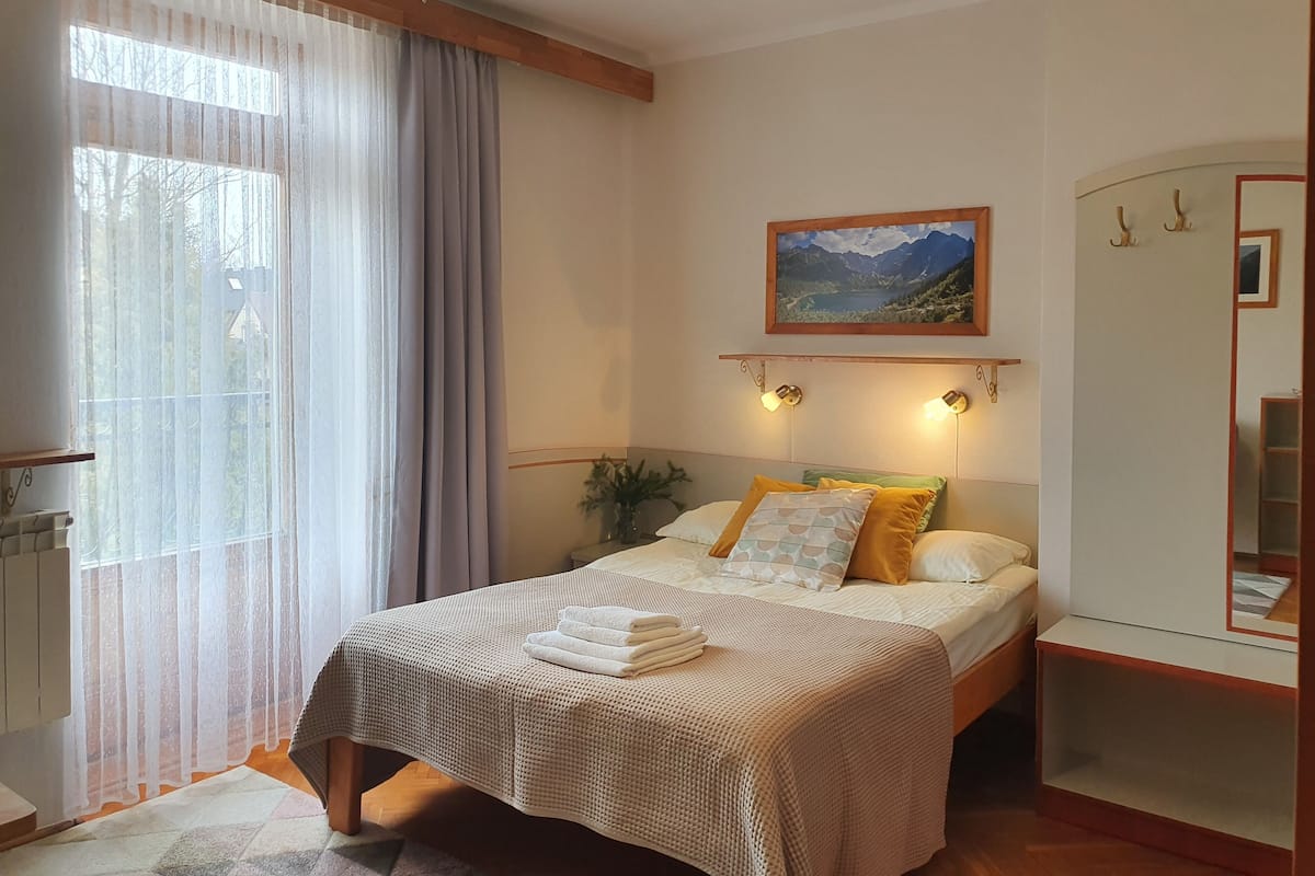A neatly arranged bedroom with a bed, a painting, and a bedside table.