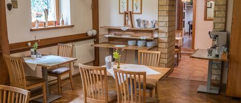 A dining area with wooden tables and chairs, a brick fireplace, and a view of the garden through a window.