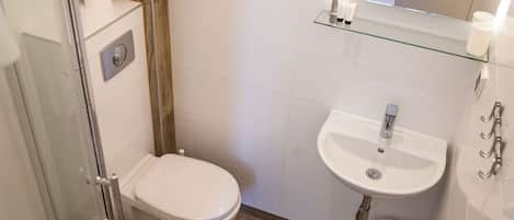 A small bathroom with a toilet, sink, and glass shelf.