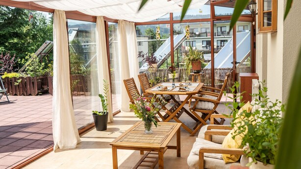 A sunlit patio with a wooden table and chairs, potted plants, and a view of a residential area. - Willa Iskra (Zakopane)