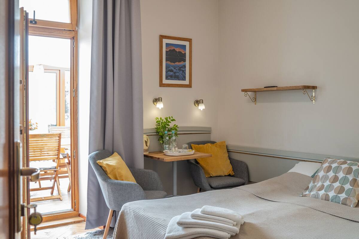 A hotel room with a bed, a desk with a plant, a chair, and a window with curtains.