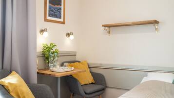 Une chambre d’hôtel comprenant un lit, deux fauteuils, une petite table avec une plante et un plateau, une étagère fixée au mur et un tableau accroché au mur.