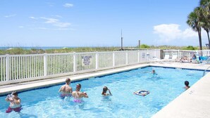 A swimming pool with a white fence, a lifeguard sign, and a view of the ocean. - Bright Beach Condo, Oceanfront Pool, Picnic Area | Crescent Sands WH - G1 (North Myrtle Beach)