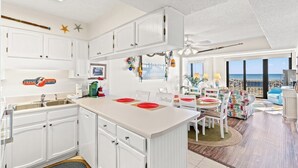 A bright kitchen with white cabinets, a central island, and a dining area with a view of the ocean. - Bright Beach Condo, Oceanfront Pool, Picnic Area | Crescent Sands WH - G1 (North Myrtle Beach)