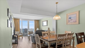 A dining area with a wooden table and chairs, a sofa, and a view through a glass door to the outside. - Clean 6th Floor Oceanfront. Pool, Sundeck, Free Wifi | Crescent Sands WH - B6 (North Myrtle Beach)