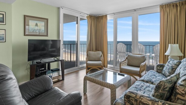 A spacious living room with a large TV, comfortable seating, and a balcony with a view of the ocean. - Clean 6th Floor Oceanfront. Pool, Sundeck, Free Wifi | Crescent Sands WH - B6 (North Myrtle Beach)