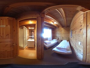 Interior de uma cabana de madeira com banheiro, duas camas e uma pequena cozinha.
