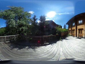 Een houten terras met een gebogen reling, een gebouw met een schuin dak en een heldere lucht.
