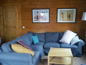 Een woonkamer met een blauwe bank, een houten salontafel en twee foto's in lijsten aan de muur.