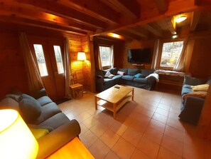A cozy cabin interior with a sofa, armchair, and a TV mounted on the wall.