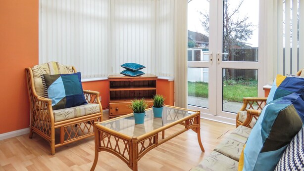 A conservatory with wicker furniture, a glass table, and a view of the outdoors. - Tudors eSuites Four Bedroom House (Birmingham)