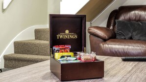A brown box with the brand name 'TWININGS' on it, placed on a wooden table in a room with a brown leather sofa and a patterned armchair. - Tudors eSuites Four Bedroom House (Birmingham)