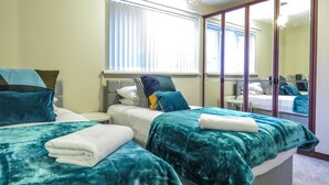 A hotel room with two beds, a large mirror, and a window with blinds. - Tudors eSuites Four Bedroom House (Birmingham)