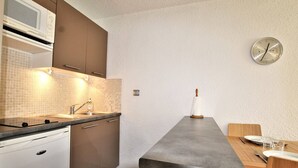 Eine moderne Küche mit eingebauter Mikrowelle, Spüle aus Edelstahl und einem Holzesstisch. An der Wand hängt eine Uhr.
