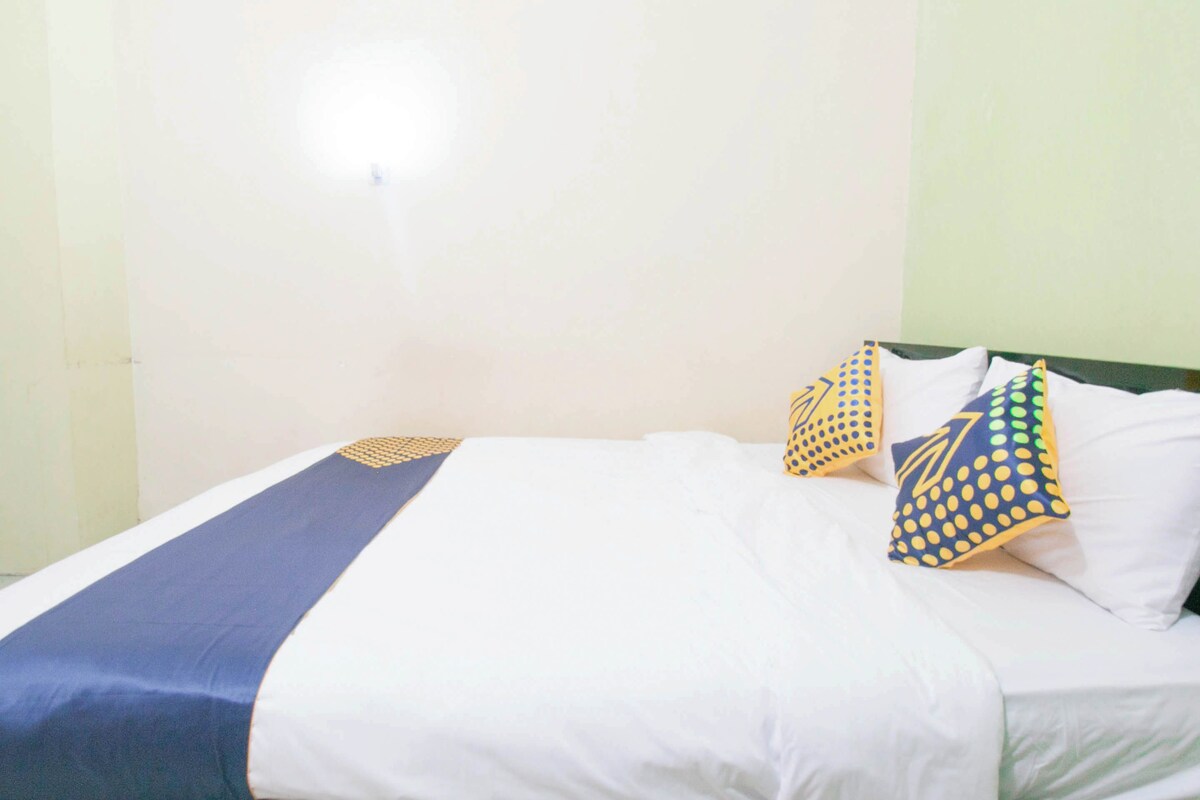 Un letto singolo con copripiumino bianco e blu, due cuscini decorati con motivi giallo e blu, e una testiera verde.