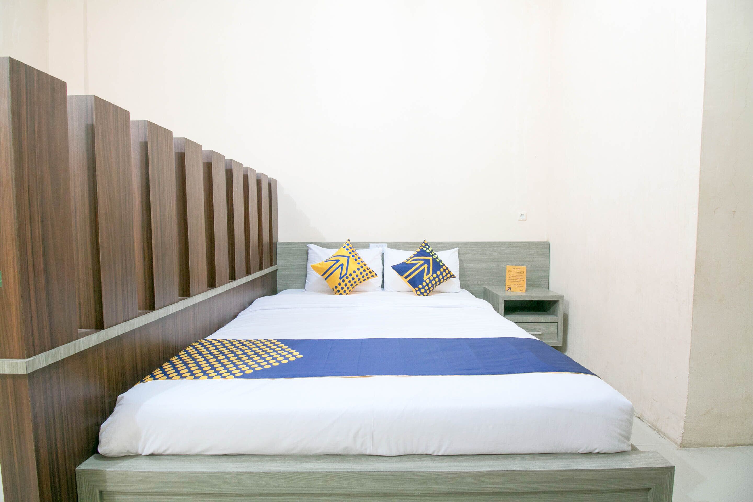A neatly made bed with a blue and yellow patterned bedspread, two pillows with geometric designs, and a wooden headboard.
