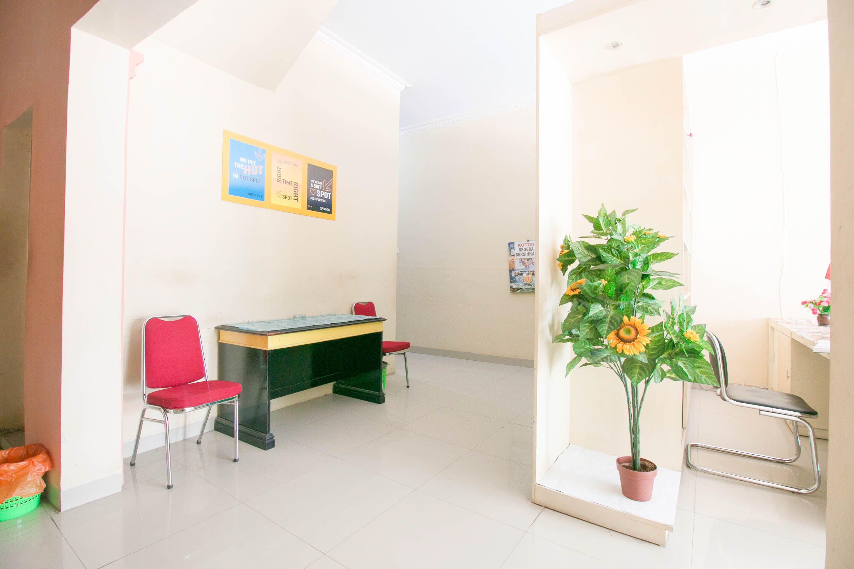 A room with a desk, two red chairs, a potted plant, and a bulletin board.