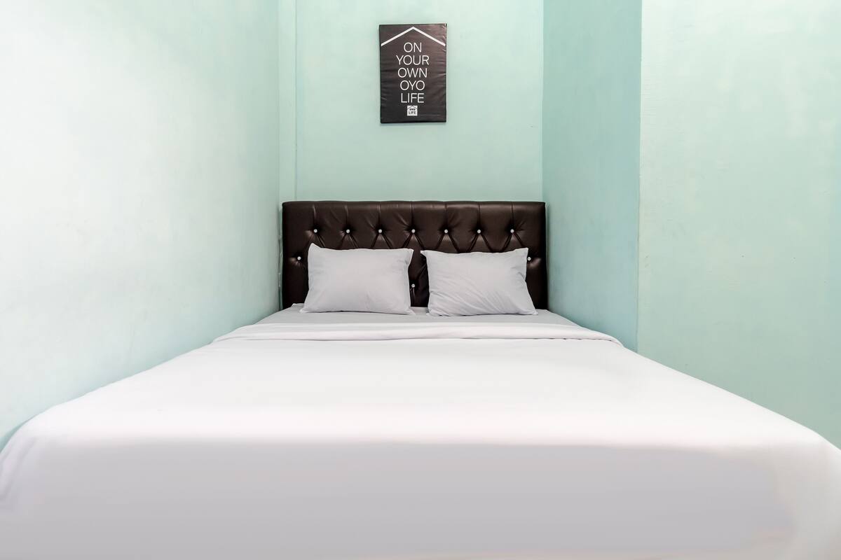 A neatly made bed with a dark headboard and white bedding in a room with light blue walls.