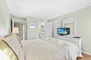 A bedroom with a bed, a television, a dresser, and a door leading to another room.