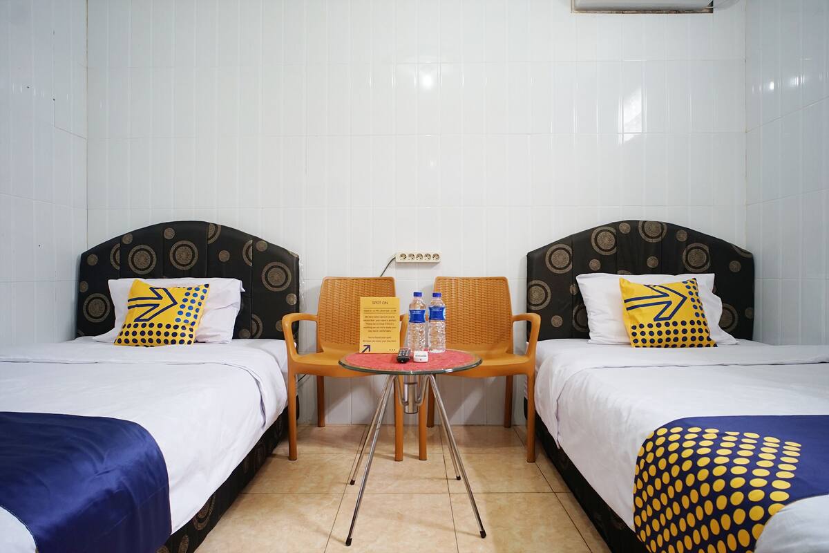 Habitación de hotel con dos camas, una mesita con sillas y un cartel que indica que la habitación está disponible.