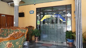 A reception area with a glass door, a sofa, potted plants, and a sign indicating the spot-on location. - SPOT ON 1854 Sepinggan Asri Syariah Guesthouse (Balikpapan)