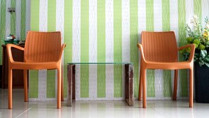 Two wicker chairs with a glass table in front of a striped wallpaper. - SPOT ON 1854 Sepinggan Asri Syariah Guesthouse (Balikpapan)