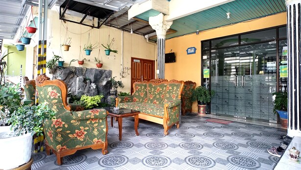A covered outdoor seating area with patterned flooring, wooden furniture, and potted plants. - SPOT ON 1854 Sepinggan Asri Syariah Guesthouse (Balikpapan)