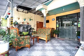 A covered outdoor seating area with patterned flooring, wooden furniture, and potted plants.
