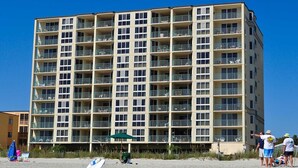 A multi-story hotel with balconies, a beach in the foreground, and a clear blue sky. - Nautical Oceanfront Condo, Outdoor Covered Heated Pool | Pinnacle - 802 (North Myrtle Beach)