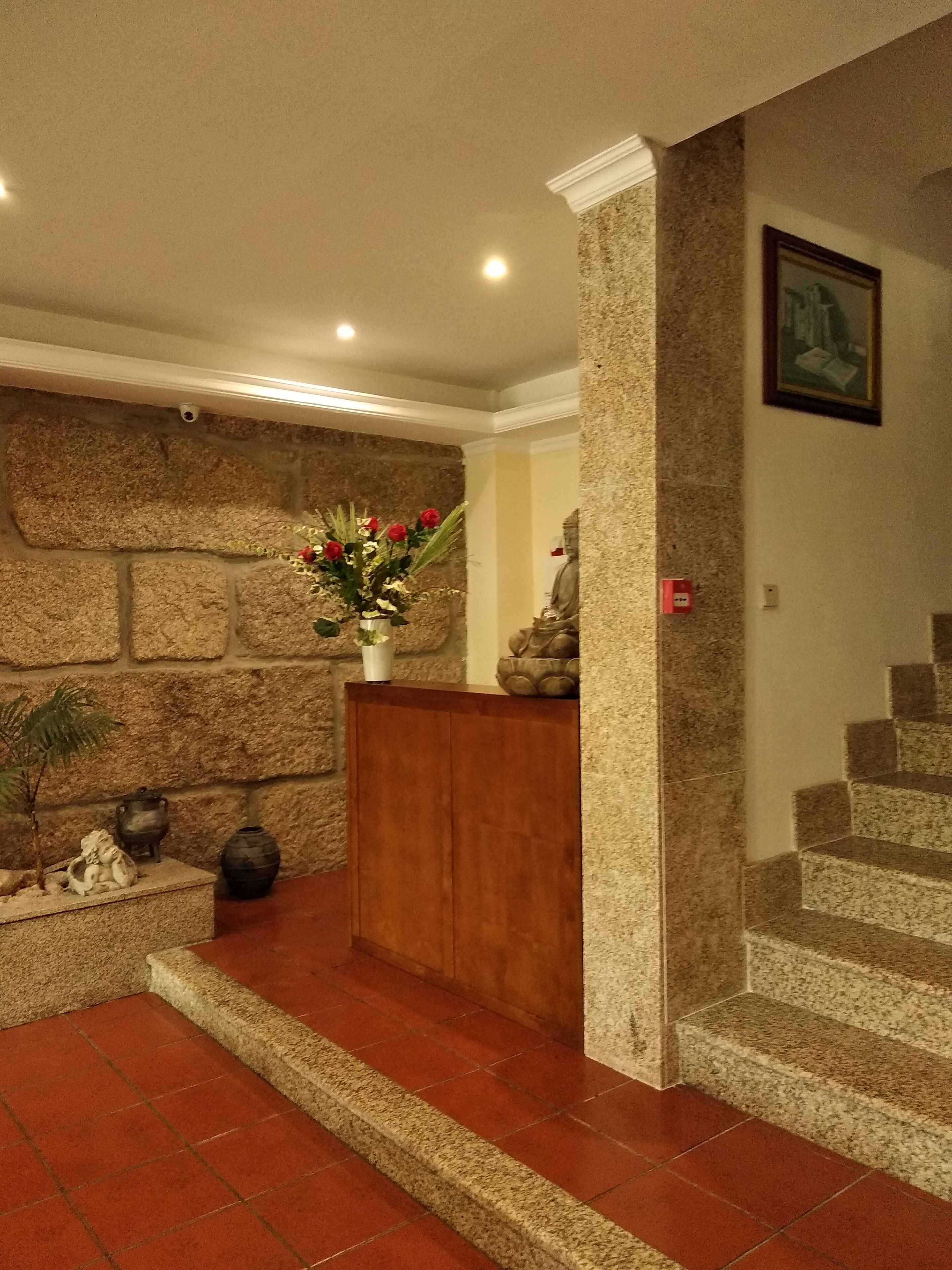 Un espace d’accueil avec un mur en pierre, un comptoir en bois, une plante en pot et un escalier.