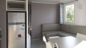 A compact kitchen with a built-in refrigerator, a dining table, and a bench. - Camping - Caravaning les Cerisiers Berck sur Mer (Verton)