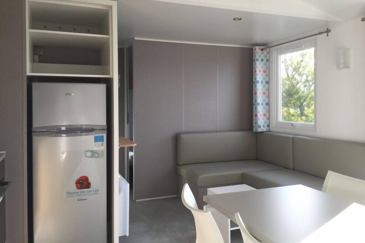A compact kitchen with a built-in refrigerator, a dining table, and a bench.