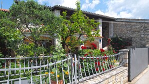 A stone-walled building with a tiled roof, surrounded by a metal fence with potted plants and flowers.