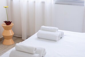 A hotel room with a bed, white towels, a potted plant, and a wooden side table.