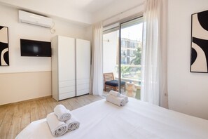 A hotel room with a bed, a flat-screen TV, a wardrobe, and a balcony with a chair and a table.