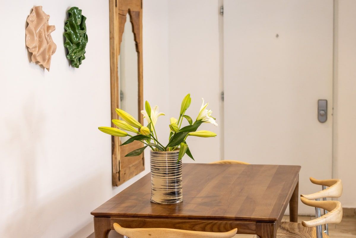 Ein Esstisch mit Blumen in einer Vase, ein Holzstuhl und ein Spiegel an der Wand.